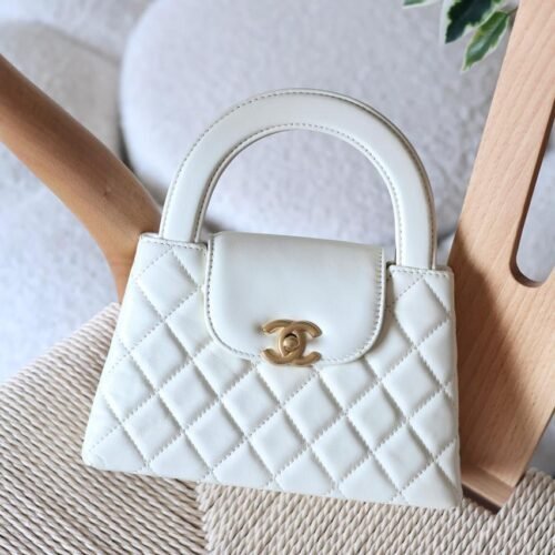 The Chanel Mini Kelly 23K in durable caviar calfskin leather boasts a rigid, compact square form with iconic quilting and antique gold CC turn-lock. Opt for hand carry with the fixed top handle or crossbody via the chain-and-leather strap. Its leather interior includes a zip pocket and slip pocket, holding iPhone 14 Pro, cards, and keys. Sleek with no back pocket, it's a versatile nano essential for everyday Chanel sophistication in Dubai.